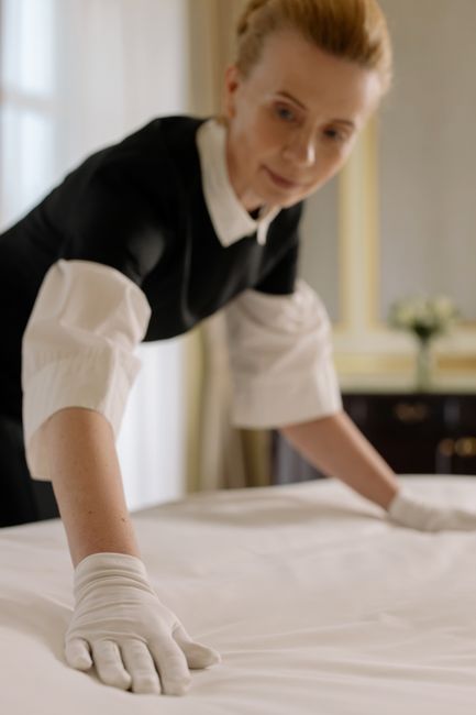 Two professional cleaners from Cleaners Richmond, dressed in red uniforms, are performing surface cleaning in a modern living room. One cleaner is using a vacuum or carpet cleaner on the dark grey til